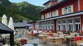 Terrasse ensoleillée du restaurant avec tables couvertes, parasols et vue sur les Alpes.