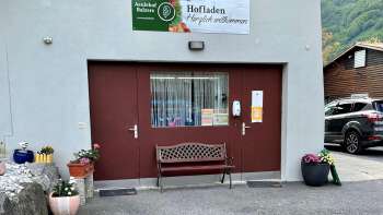 Entrée de la boutique de la ferme Aeulehof avec portail rouge, banc et décoration florale à Triesen, Liechtenstein.