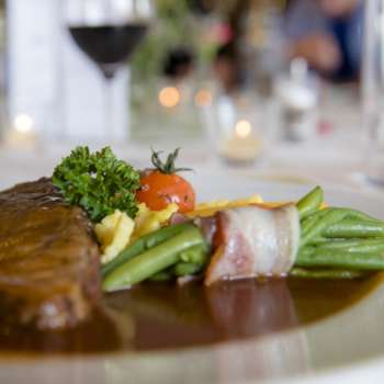 Détail d'un plat principal avec des légumes verts, du bacon et une sauce crémeuse dans l'assiette