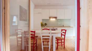 Salle de séjour et salle à manger lumineuse avec kitchenette moderne et chaises rouges et blanches dans la maison d'hôtes au camping Mittagsspitze.