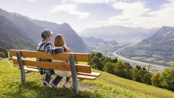 Deux randonneurs sont assis sur un banc et profitent de la vue sur la vallée du Rhin.