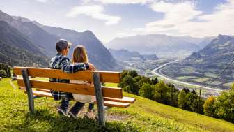 Couple assis sur un banc à Triesenberg et regardant la vallée du Rhin au Liechtenstein avec un panorama alpin impressionnant