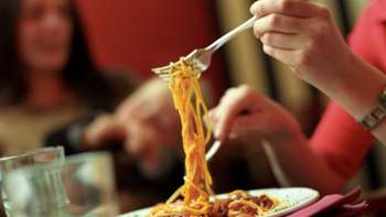 Une personne prend des spaghettis avec une fourchette dans une assiette à la Brasserie Burg - un plaisir italien dans une atmosphère conviviale.