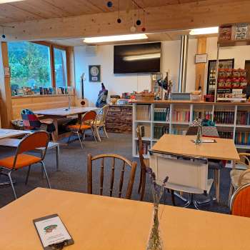 Vue sur la salle de restaurant avec mur en bois et décoration murale - Plusieurs tables avec sièges et vue sur le mur décoratif avec des guitares et des tableaux verts.