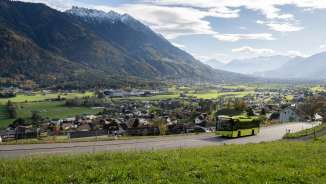 Le bus vert LIEmobil emprunte une route sinueuse au-dessus du Liechtenstein avec vue sur la vallée du Rhin et les Alpes environnantes.
