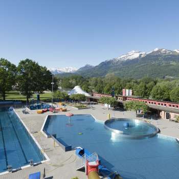 Vue générale de la piscine en plein air de Mühleholz avec plusieurs bassins et un magnifique panorama alpin en arrière-plan.