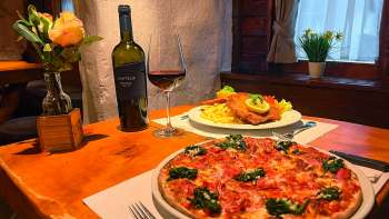 Gros plan d'une pizza à la tomate, au fromage et au basilic sur une table en bois, avec un verre de vin rouge en arrière-plan.