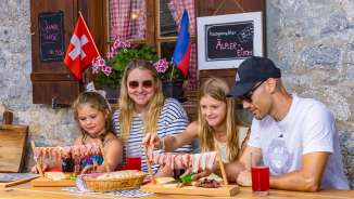 Famille assise sur un alpage ensoleillé du Liechtenstein, savourant une collation traditionnelle avec des spécialités régionales et un panorama de montagne.