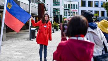 Une guide portant le drapeau du Liechtenstein accueille un groupe de touristes à Vaduz