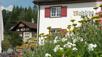 Auberge de montagne traditionnelle avec volet rouge et fleurs épanouies au premier plan Auberge de montagne traditionnelle avec volet rouge et fleurs épanouies au premier plan