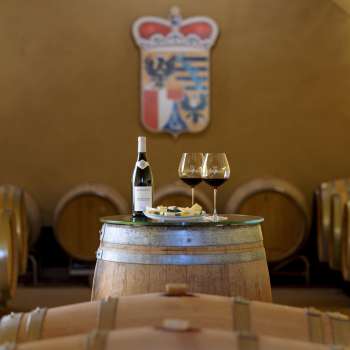Dégustation de vin d'ambiance dans la cave à vin du domaine princier avec deux verres et une bouteille de vin rouge sur un tonneau en bois.