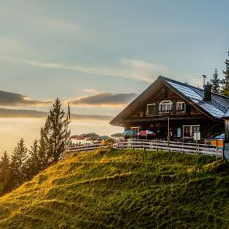 refuge de Gafadura sur une colline verdoyante au Liechtenstein au coucher du soleil avec vue panoramique sur les montagnes