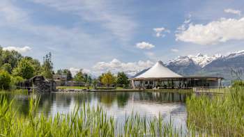 Pavillon moderne au bord de l'eau dans le parc de loisirs de Grossabünt au Liechtenstein, entouré de nature et avec vue sur les Alpes.