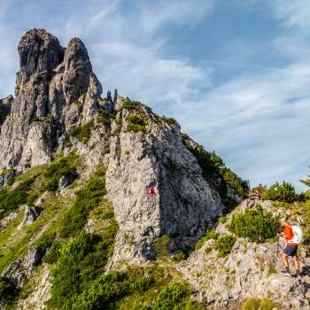 Randonneurs sur un sentier de montagne rocheux devant une arête déchiquetée avec un panneau de signalisation rouge et blanc