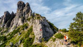 Randonneurs sur un sentier de montagne rocheux devant une arête déchiquetée avec un panneau de signalisation rouge et blanc