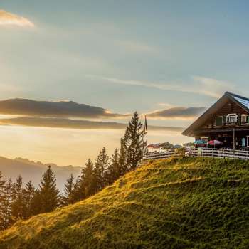 Cabane de Gadafura sur une prairie de montagne ensoleillée avec vue sur les montagnes et le coucher du soleil