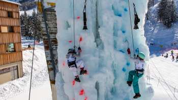 Deux enfants escaladent la glace sur la tour d'escalade gelée de Malbun avec des piolets et des casques