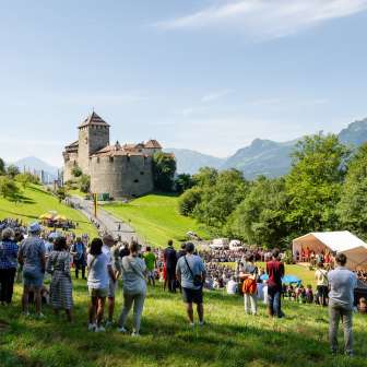 Les visiteurs se rassemblent pour l'acte d'État 2024 au Liechtenstein sur la pelouse en dessous du château de Vaduz