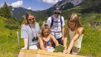 La famille explore une station interactive sur le sentier thématique de Malbun, entouré de paysages alpins et de prairies d'été au Liechtenstein.