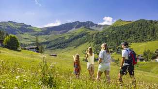 Une famille se promène dans une prairie d'été fleurie à Malbun, au Liechtenstein, en admirant la vue sur les Alpes environnantes.