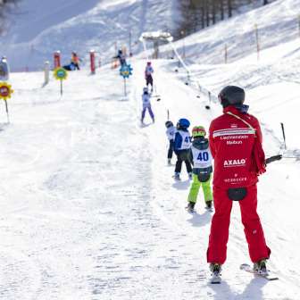 Un moniteur de ski accompagne les enfants sur le téléski d'entraînement de Malbun - domaine skiable idéal pour les familles et les débutants au Liechtenstein.