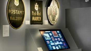 Salle du musée avec d'anciennes plaques postales et un affichage numérique sur l'histoire de la poste au Liechtenstein.