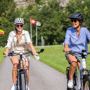 Deux femmes sur des vélos électriques lors d'un tour estival avec les drapeaux du Liechtenstein, de la Suisse et de l'Autriche en arrière-plan