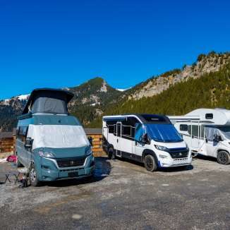 Plusieurs campeurs et camping-cars sur un emplacement dans les montagnes du Liechtenstein sous un ciel bleu éclatant