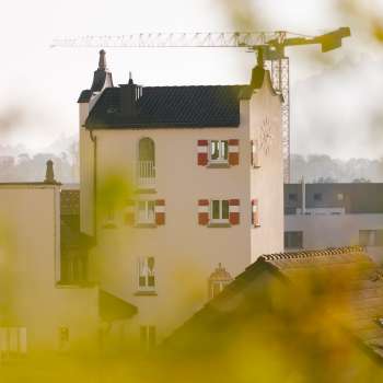 Gros plan sur la tour historique de l'hôtel de ville de Vaduz avec ses remarquables volets rouges, entourée de grues de chantier en arrière-plan.