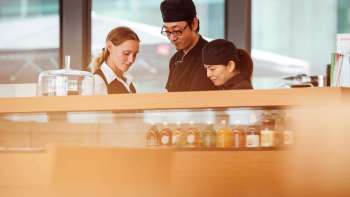 Trois employés du café du Musée des Beaux-Arts travaillant ensemble au comptoir et se concentrant sur leurs échanges.