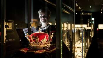 Une jeune femme regarde une somptueuse couronne derrière une vitre au musée national du Liechtenstein.