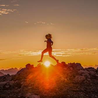 Deux coureurs de trail traversent une crête rocheuse au lever du soleil au Liechtenstein, dans la lumière dorée de l'aube.