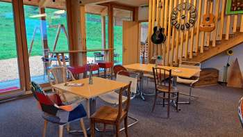 Salle de restaurant confortable avec des éléments en bois - La salle de restaurant est aménagée avec des meubles en bois clair et des guitares décoratives au mur, ambiance chaleureuse grâce à la lumière naturelle.