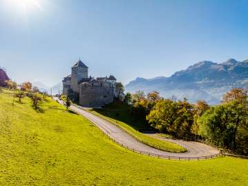 Vue du château de Vaduz au Liechtenstein avec des arbres automnaux et un soleil radieux