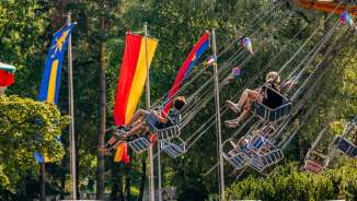 Enfants et adultes montent sur un carrousel à chaînes à la fête foraine de Balzers, entourés de drapeaux colorés, sous le soleil.
