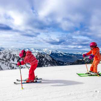 Deux enfants font du ski à Sareis, avec vue sur les montagnes enneigées et le paysage hivernal.