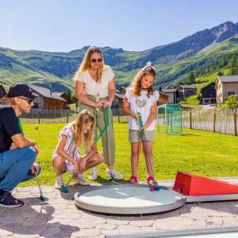 Une famille joue au minigolf ensemble dans le village de montagne ensoleillé de Malbun au Liechtenstein - un plaisir pour petits et grands dans les Alpes.