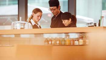 Trois employés du café du Musée des Beaux-Arts travaillant ensemble au comptoir et se concentrant sur leurs échanges.