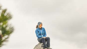 Rosaria Michaela Ackermann est assise sur une pierre dans les montagnes du Liechtenstein et regarde au loin.