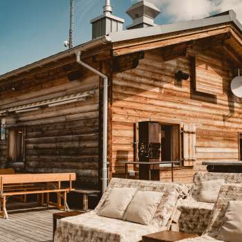Agréable terrasse ensoleillée avec des bancs en bois et des meubles de salon confortables devant le refuge Sareis à 2.000 mètres d'altitude, sous un soleil radieux et dans un décor de montagne.