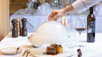 Plat gastronomique servi avec viande et garniture, présenté de manière décorative sous une cloche blanche dans le restaurant raffiné Alpspitz.