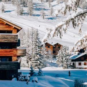 Chalets confortables dans la station de sports d'hiver de Malbun entourés d'arbres enneigés et de pistes de ski en arrière-plan