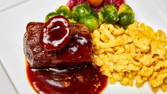 Plat traditionnel de gibier avec spätzle et choux de Bruxelles Délicieux plat de gibier avec sauce foncée, spätzle dorés, choux de Bruxelles et airelles rouges dressés sur une assiette blanche.
