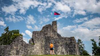 Une randonneuse se tient devant les ruines imposantes du château de Schellenberg sous un ciel bleu