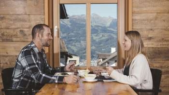 Un couple savoure un repas convivial avec vue sur les montagnes dans un décor rustique en bois