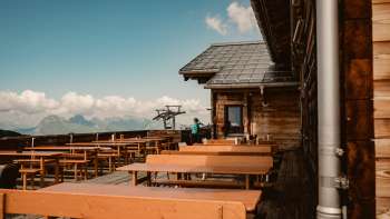 Bancs en bois vides sur la terrasse panoramique de la cabane Sareis avec vue sur les Alpes - idéal pour une pause pendant une randonnée ou un trajet en téléphérique.