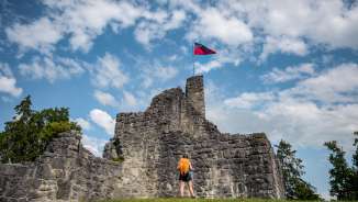 Randonneuse devant les ruines historiques du château de Schellenberg avec le drapeau du Liechtenstein flottant sous un ciel bleu