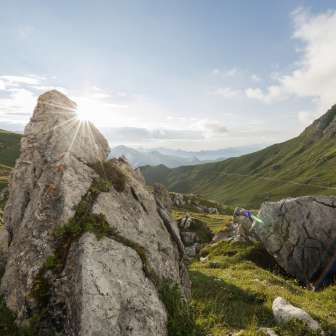 Lever de soleil derrière des formations rocheuses dans la vallée verdoyante de la Naaftal au Liechtenstein, entourée de douces collines et d'un paysage montagneux