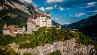 L'imposant château de Gutenberg trône sur un rocher à Balzers, entouré de pentes verdoyantes et d'un majestueux décor alpin sous un ciel bleu.