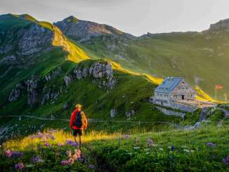 Un randonneur regarde le refuge Pfälzerhütte au Liechtenstein, entouré d'un paysage de montagnes verdoyantes et d'un panorama alpin au crépuscule.